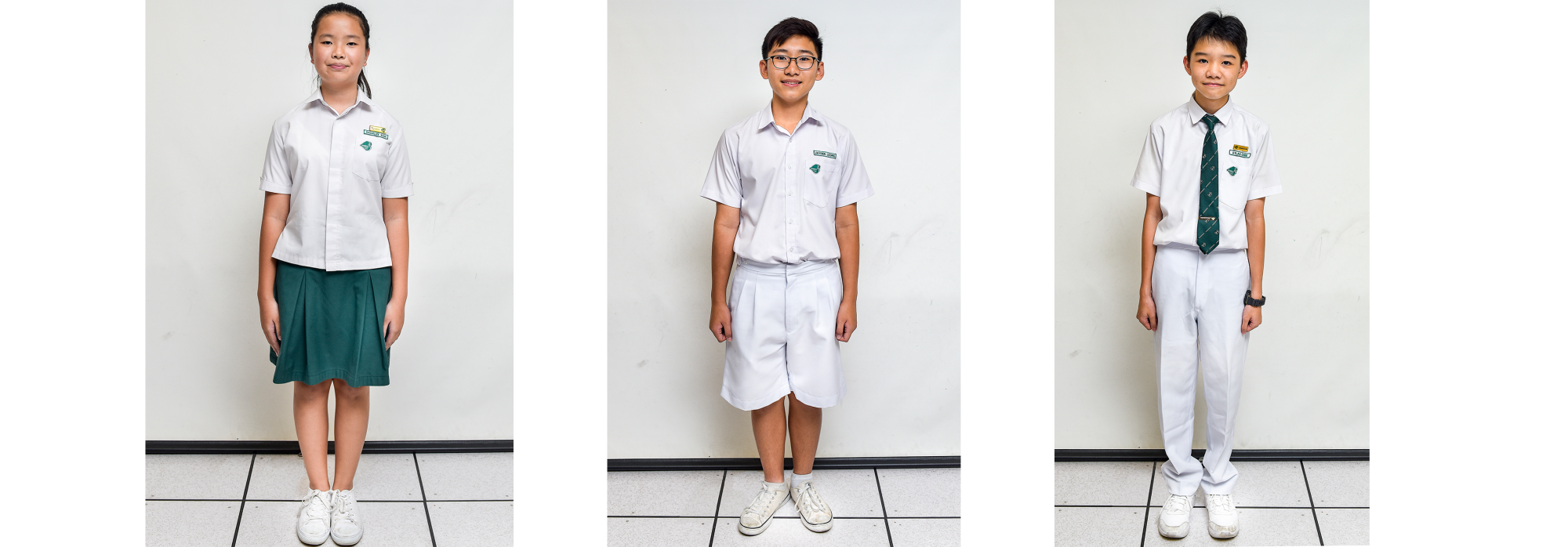 Three students in school uniforms: a girl in white shirt and green skirt, two boys in white shirts and pants or shorts.